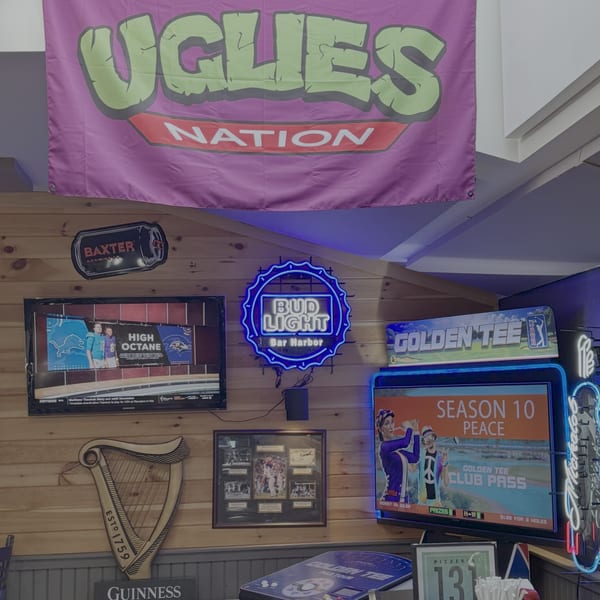 A wall with various signs, including a Bud Light neon sign, a Golden Tee arcade game, and a Guinness harp.