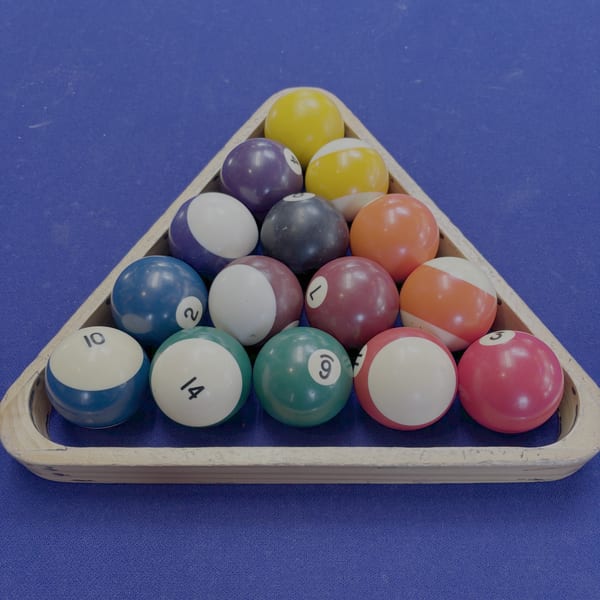 A triangular rack of colorful billiard balls on a blue pool table at Pizzeria 131.