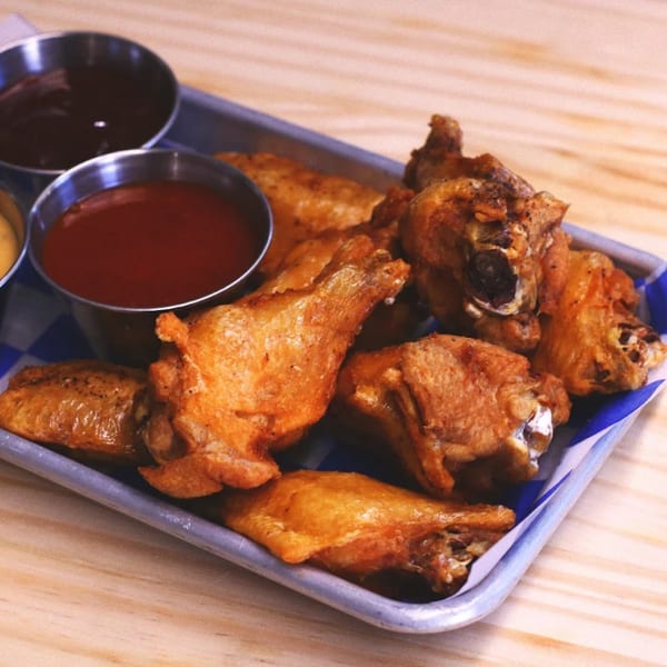 Crispy fried chicken wings on a metal tray with blue and white checkered paper, served with dipping sauces.