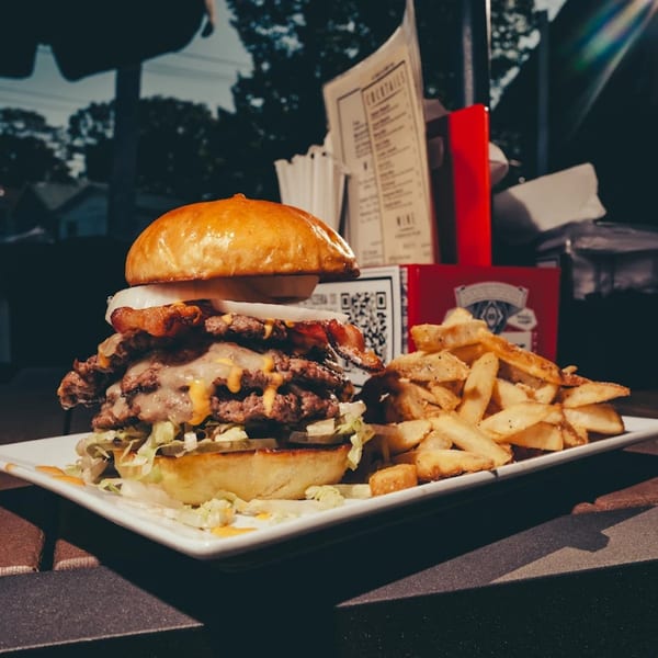 A large Pizzeria 131 burger with cheese, bacon, and onions, served with a side of fries.