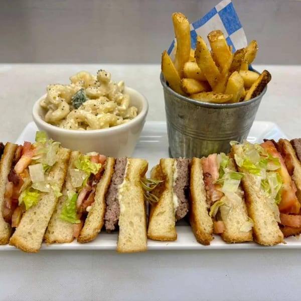 A platter with a club sandwich, a side of macaroni salad, and a bucket of french fries.
