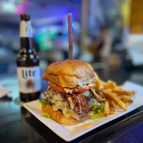 A Pizzeria 131 burger with bacon, cheese, tomato, and lettuce, served with fries and a beer.